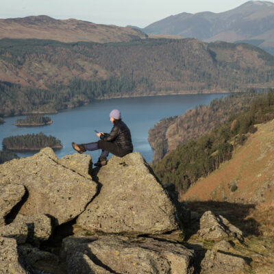A woman sitting on a rock high above a lake